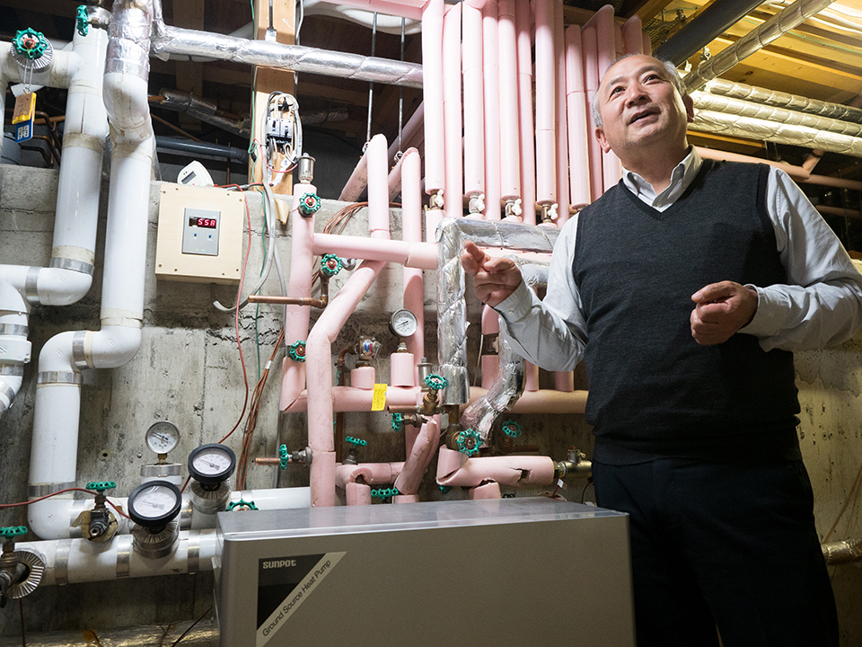 写真：ヒートポンプの前に立つ社長・土屋隆幸